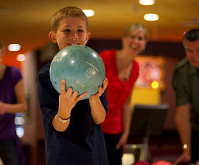 a young boy bowling as his family encourages him