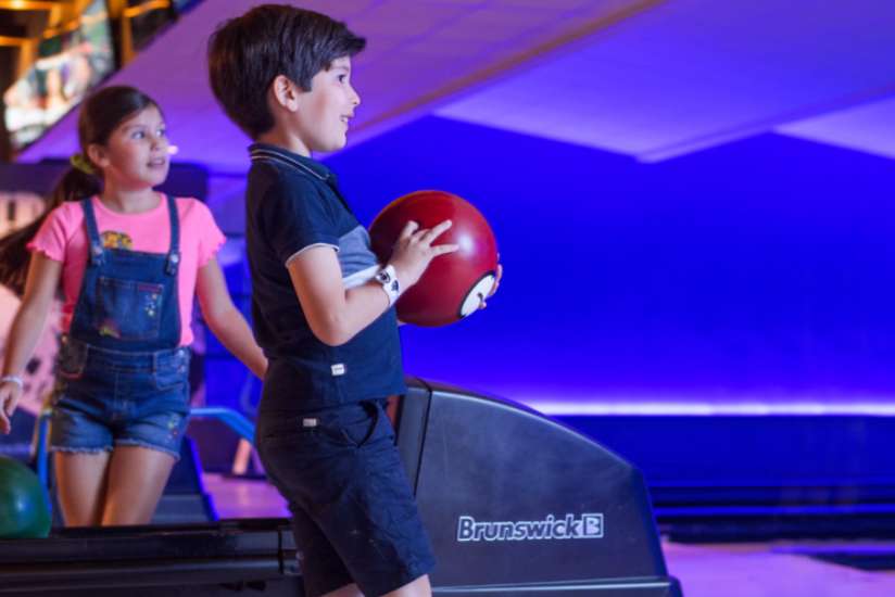 Young boy getting ready to throw his bowling ball down the alley while dad and sister patiently watch.